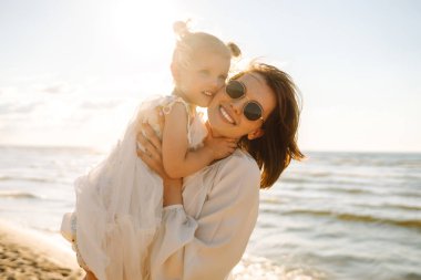 Neşeli anne ve kız gün batımı kumsalında birlikte eğleniyorlar. Küçük kızı olan güzel bir kadın dışarıda birlikte vakit geçiriyor. Çocukluk, eğlence, rahatlama konsepti.