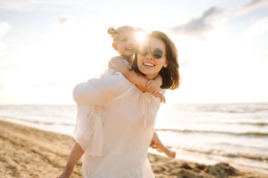 Neşeli anne ve kız gün batımı kumsalında birlikte eğleniyorlar. Küçük kızı olan güzel bir kadın dışarıda birlikte vakit geçiriyor. Çocukluk, eğlence, rahatlama konsepti.