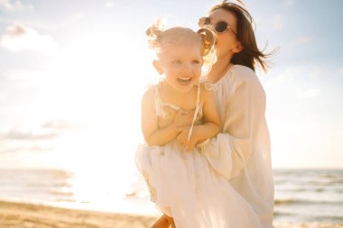 Neşeli anne ve kız gün batımı kumsalında birlikte eğleniyorlar. Küçük kızı olan güzel bir kadın dışarıda birlikte vakit geçiriyor. Çocukluk, eğlence, rahatlama konsepti.