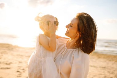 Neşeli anne ve kız gün batımı kumsalında birlikte eğleniyorlar. Küçük kızı olan güzel bir kadın dışarıda birlikte vakit geçiriyor. Çocukluk, eğlence, rahatlama konsepti.