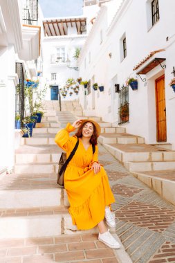 Şapkalı ve parlak elbiseli hoş bir kadın şehrin parlak caddelerinde yürüyor. Sırt çantalı güzel bir kadın yolculuğun tadını çıkarıyor. Turizm, yürüyüş konsepti. Etkin yaşam biçimi.