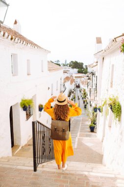 Şapkalı ve parlak elbiseli hoş bir kadın şehrin parlak caddelerinde yürüyor. Sırt çantalı güzel bir kadın yolculuğun tadını çıkarıyor. Turizm, yürüyüş konsepti. Etkin yaşam biçimi.