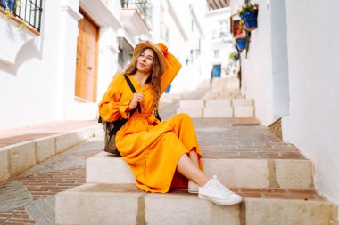 Şapkalı ve parlak elbiseli hoş bir kadın şehrin parlak caddelerinde yürüyor. Sırt çantalı güzel bir kadın yolculuğun tadını çıkarıyor. Turizm, yürüyüş konsepti. Etkin yaşam biçimi.