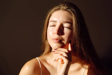 Güneş ışınlarında eli ile tenine dokunan genç bir kadının portresi. Cildiyle ilgilenen güzel bir kadın, ev atmosferinin tadını çıkarıyor. Güzellik, cilt bakımı.