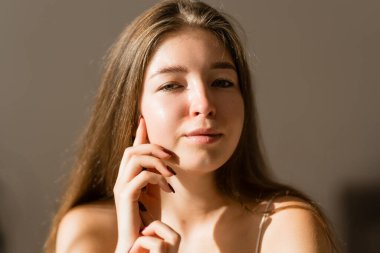 Güneş ışınlarında eli ile tenine dokunan genç bir kadının portresi. Cildiyle ilgilenen güzel bir kadın, ev atmosferinin tadını çıkarıyor. Güzellik, cilt bakımı.