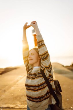 Arka planda deniz feneri olan mutlu bir kadın rıhtımda eğleniyor. Gün batımında özgür hisseden güzel bir kadın. Macera, yürüyüş konsepti. Yaşam biçimi.