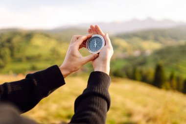 Pusulayla turistin elini yakın plan çek. Gezgin yön arıyor ve gün batımında yeşil tepede pusula ile yürüyüş rotasını seçiyor. Seyahat konsepti, seyrüsefer, özgürlük.