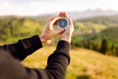 Pusulayla turistin elini yakın plan çek. Gezgin yön arıyor ve gün batımında yeşil tepede pusula ile yürüyüş rotasını seçiyor. Seyahat konsepti, seyrüsefer, özgürlük.