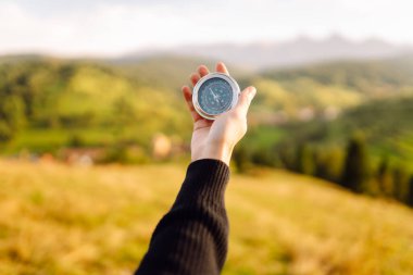 Pusulayla turistin elini yakın plan çek. Gezgin yön arıyor ve gün batımında yeşil tepede pusula ile yürüyüş rotasını seçiyor. Seyahat konsepti, seyrüsefer, özgürlük.