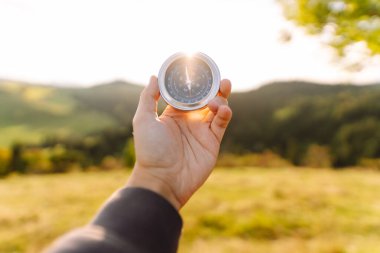 Pusulayla turistin elini yakın plan çek. Gezgin yön arıyor ve gün batımında yeşil tepede pusula ile yürüyüş rotasını seçiyor. Seyahat konsepti, seyrüsefer, özgürlük.