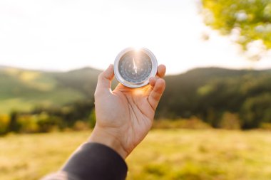 Pusulayla turistin elini yakın plan çek. Gezgin yön arıyor ve gün batımında yeşil tepede pusula ile yürüyüş rotasını seçiyor. Seyahat konsepti, seyrüsefer, özgürlük.