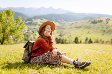 Sırt çantalı genç bir kadın yeşil bir tepede yürüyor. Şapkalı bir bayan gezgin güneşli havanın tadını çıkarıyor, özgür hissediyor. Macera konsepti, özgürlük. Etkin yaşam biçimi.