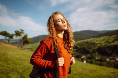 Sırt çantalı genç bir kadın yeşil bir tepede yürüyor. Şapkalı bir bayan gezgin güneşli havanın tadını çıkarıyor, özgür hissediyor. Macera konsepti, özgürlük. Etkin yaşam biçimi.