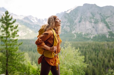 Parlak bir sırt çantası olan aktif bir bayan gezgin uçurumdan dağ manzarasının keyfini çıkarıyor. Genç bir kadın yürüyüş yaparken özgürlüğünü hissediyor. Macera konsepti.