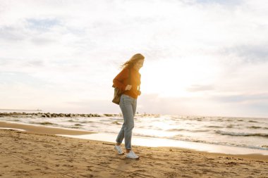 Sırt çantalı kadın gezginin gün batımında kumlu sahilde yürüyüşü. Deniz kıyısında özgürlük hisseden genç bir kadın. Özgürlük, seyahat kavramı.