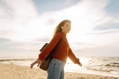 Sırt çantalı kadın gezginin gün batımında kumlu sahilde yürüyüşü. Deniz kıyısında özgürlük hisseden genç bir kadın. Özgürlük, seyahat kavramı.