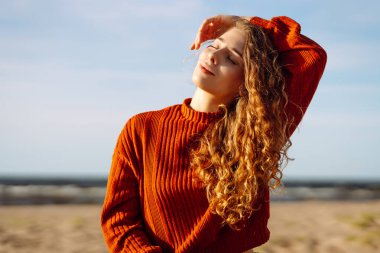 Güneşli sahilde rüzgarın tadını çıkaran rahat kadın portresi. Güzel bir kadın denizin yanında özgürlüğünü hisseder. Keyif, rahatlama, özgürlük kavramı.