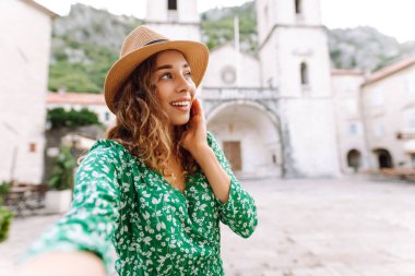 Şirin turist güzel mimari binaların arka planında selfie çekiyor. Genç bir kadın yeni Avrupa caddelerinde yürümekten hoşlanıyor. Selfie, blog ve turizm konsepti.