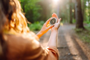 Yürüyüşçünün ellerinin bir orman patikasına karşı pusula tutarken yakın plan görüntüsü. Dişi bir yürüyüşçü yürüyüş parkurunda bir pusula ile arazide gezinir. Macera ve eğlence konsepti.