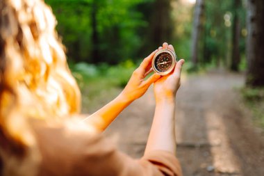 Yürüyüşçünün ellerinin bir orman patikasına karşı pusula tutarken yakın plan görüntüsü. Dişi bir yürüyüşçü yürüyüş parkurunda bir pusula ile arazide gezinir. Macera ve eğlence konsepti.
