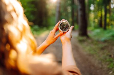 Yürüyüşçünün ellerinin bir orman patikasına karşı pusula tutarken yakın plan görüntüsü. Dişi bir yürüyüşçü yürüyüş parkurunda bir pusula ile arazide gezinir. Macera ve eğlence konsepti.