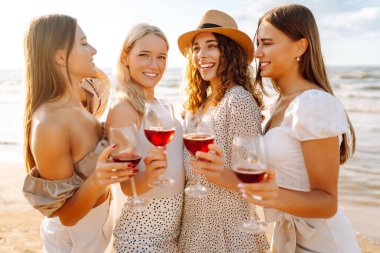 Genç bayan arkadaşlar sahilde şarap kadehleriyle eğleniyorlar. Açık havada eğlenen dört güzel kadın. Arkadaşlık, rahatlık, piknik konsepti. Yaşam biçimi.