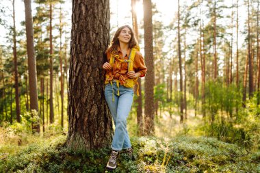 Sarı sırt çantalı kadın yürüyüşçü güneşli ormanda yürürken günışığının tadını çıkarıyor. Yürüyüş yolunda genç bir kadın yürüyüşçü. Turizm, yürüyüş konsepti.