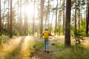 Sarı sırt çantalı kadın yürüyüşçü güneşli ormanda yürürken günışığının tadını çıkarıyor. Yürüyüş yolunda genç bir kadın yürüyüşçü. Turizm, yürüyüş konsepti.