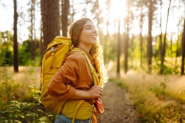 Sarı sırt çantalı kadın yürüyüşçü güneşli ormanda yürürken günışığının tadını çıkarıyor. Yürüyüş yolunda genç bir kadın yürüyüşçü. Turizm, yürüyüş konsepti.