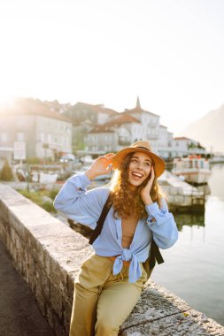 Şapkalı neşeli turist setin üzerinde güneşin doğuşunun tadını çıkarıyor. Genç bir kadın güzel bir mimarisi olan şirin bir köyde yürüyor. Turizm, seyahat konsepti. Etkin yaşam biçimi.