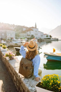 Şapkalı neşeli turist setin üzerinde güneşin doğuşunun tadını çıkarıyor. Genç bir kadın güzel bir mimarisi olan şirin bir köyde yürüyor. Turizm, seyahat konsepti. Etkin yaşam biçimi.