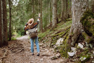 Sırt çantalı genç bir turist dağ ormanlarında yürüyüş yolu boyunca yürüyor. Mutlu kadın açık havayı seviyor. Yürüyüş, seyahat konsepti. Etkin yaşam biçimi.