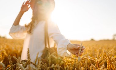Gün batımı tarlasında altın buğdaya dokunan genç bir kadının elleri. Tarlada gezen şık elbiseli güzel bir kadın. Yürüme ve eğlenme kavramı.