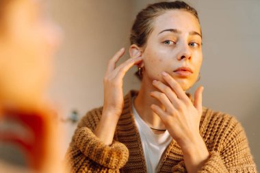 Yüzüne nemlendirici süren genç bir kadının portresi. Güzel bir kadın aynadaki kusurlarını inceliyor. Güzellik ve doğallık kavramı.