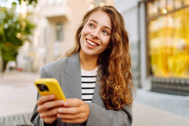 Şık giyinmiş güzel bir kadın elinde telefonla günbatımı caddelerinde yürüyor. Telefonu olan genç bir turist blog çekiyor ve açık havanın tadını çıkarıyor. Bloglama, güzellik konsepti.