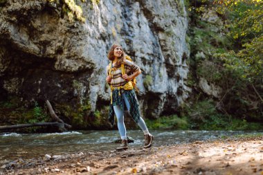 Dağlarda dağ nehrinin yanında yürüyüş yapan sarı sırt çantalı genç bir kadın. Mutlu bayan gezgin açık havada güneşli havanın tadını çıkarıyor. Seyahat konsepti, yürüyüş. Etkin yaşam biçimi.