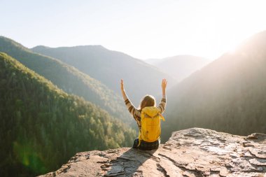 Renkli sırt çantalı mutlu bayan gezgin dağ manzarasının tadını çıkarıyor. Uçurumun kenarında duran genç kadın özgürlüğü hissediyor. Macera konsepti, özgürlük. Seyahat tutkusu.