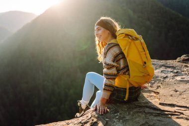 Renkli sırt çantalı mutlu bayan gezgin dağ manzarasının tadını çıkarıyor. Uçurumun kenarında duran genç kadın özgürlüğü hissediyor. Macera konsepti, özgürlük. Seyahat tutkusu.