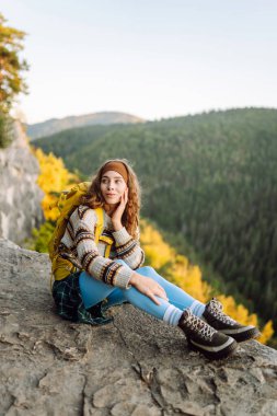 Renkli sırt çantalı mutlu bayan gezgin dağ manzarasının tadını çıkarıyor. Uçurumun kenarında duran genç kadın özgürlüğü hissediyor. Macera konsepti, özgürlük. Seyahat tutkusu.