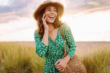 Kumsalda uzun otların yanında yürüyen mutlu bir kadın. Uçan saçlar. Açık havada. Moda tarzı