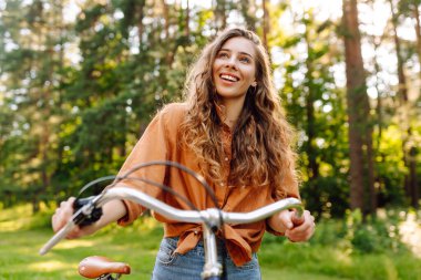 Genç modern kadın parkta bisiklet sürüyor. Spor aktiviteleri. Çevreyle ilgilenmek