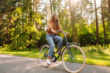 Genç modern kadın parkta bisiklet sürüyor. Spor aktiviteleri. Çevreyle ilgilenmek