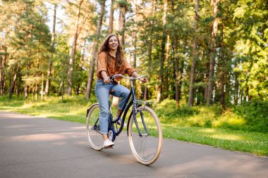 Genç modern kadın parkta bisiklet sürüyor. Spor aktiviteleri. Çevreyle ilgilenmek