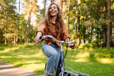 Genç modern kadın parkta bisiklet sürüyor. Spor aktiviteleri. Çevreyle ilgilenmek