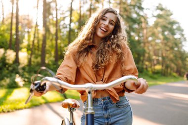 Genç modern kadın parkta bisiklet sürüyor. Spor aktiviteleri. Çevreyle ilgilenmek
