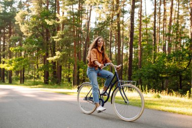 Genç modern kadın parkta bisiklet sürüyor. Spor aktiviteleri. Çevreyle ilgilenmek