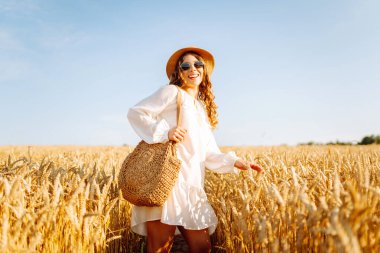 Sarı buğday tarlasında koşan mutlu kadın tatillerde kırsal alanda özgürlüğün tadını çıkarıyor. Dinlen, köyde dinlen, gün batımında köy