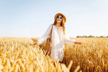 Sarı buğday tarlasında koşan mutlu kadın tatillerde kırsal alanda özgürlüğün tadını çıkarıyor. Dinlen, köyde dinlen, gün batımında köy