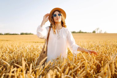 Sarı buğday tarlasında koşan mutlu kadın tatillerde kırsal alanda özgürlüğün tadını çıkarıyor. Dinlen, köyde dinlen, gün batımında köy