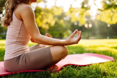 Sabah yogası. Spor giyim bölümünde genç ve güzel bir kadın parktaki spor minderinde vücut esnetiyor, yoga yapıyor. Sağlıklı yaşam tarzı, spor.